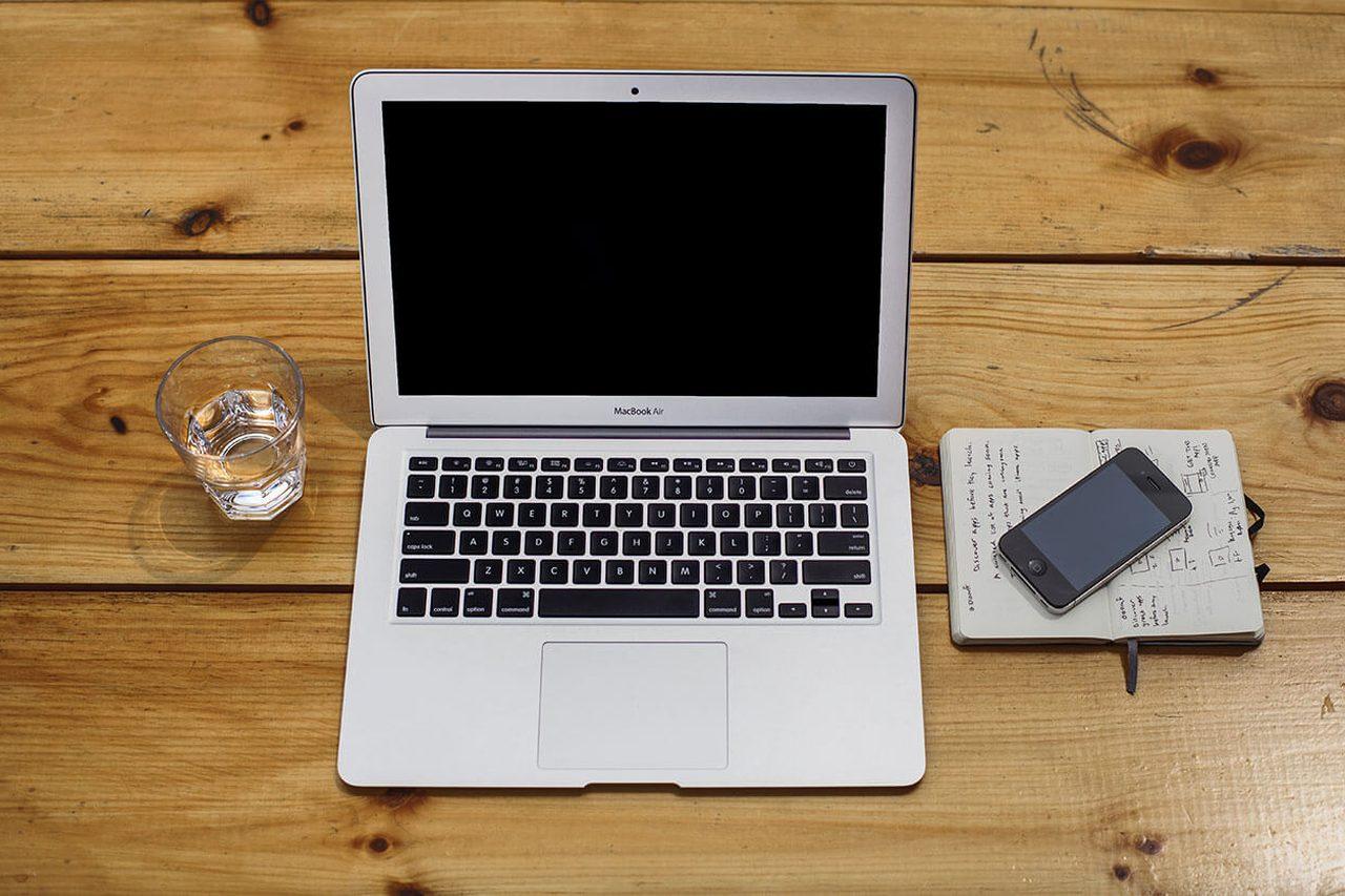 A MacBook, notebook and phone laid out on a wooden desk