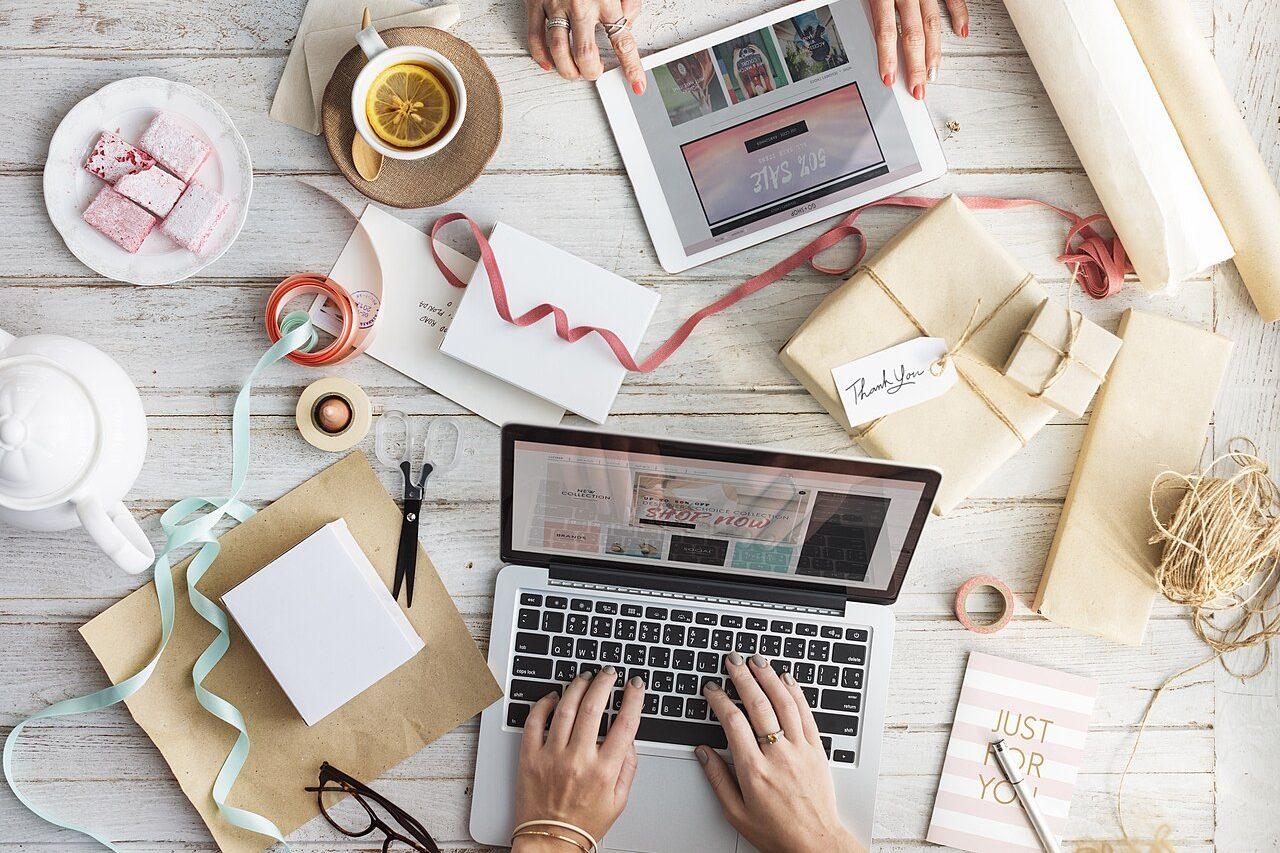 A flat lay of wrapped gifts, ribbon and a laptop on a desk