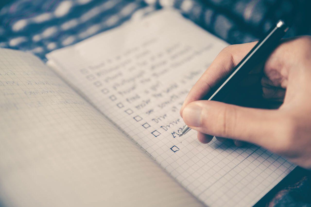 A hand writing a checklist by hand in a notebook